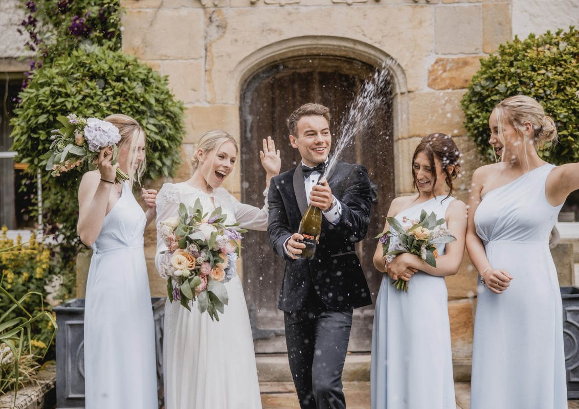 Groom celebrates with champagne at Lartington Hall wedding venue. 